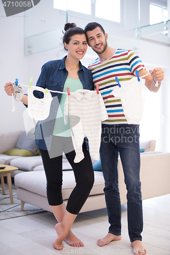 Image of young couple holding baby bodysuits at home