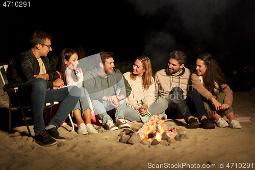Image of group of friends sitting at camp fire on beach