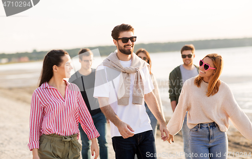 Image of happy friends walking along summer beach