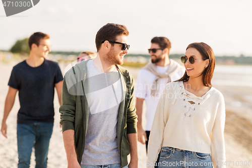 Image of happy friends walking along summer beach