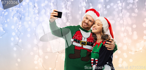 Image of happy couple in christmas sweaters taking selfie