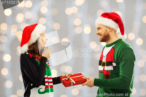 Image of happy couple in christmas sweaters with gift box