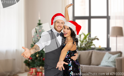 Image of happy couple in santa hats at home on christmas