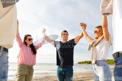 Image of happy friends holding hands on summer beach