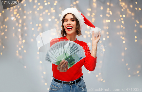 Image of happy woman in santa hat with money on christmas