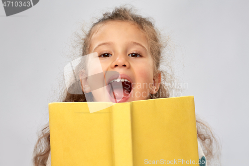 Image of happy little girl hiding behind yellow book