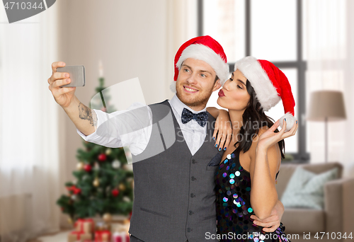 Image of couple in santa hats taking selfie on christmas