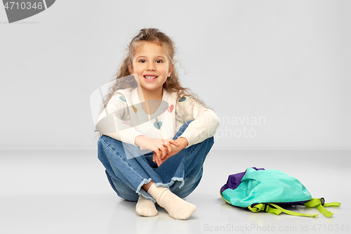 Image of happy little girl with school bag sitting on floor