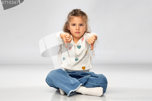Image of sad girl sitting on floor and showing thumbs down