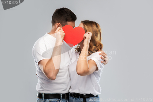 Image of smiling couple kissing behind big red heart