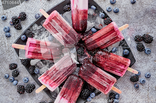 Image of Homemade fresh frozen blueberry and blackberry popsicles on black plate with ice sitting on stone