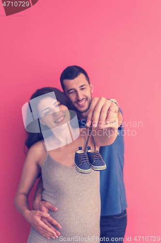 Image of young pregnant couple holding newborn baby shoes