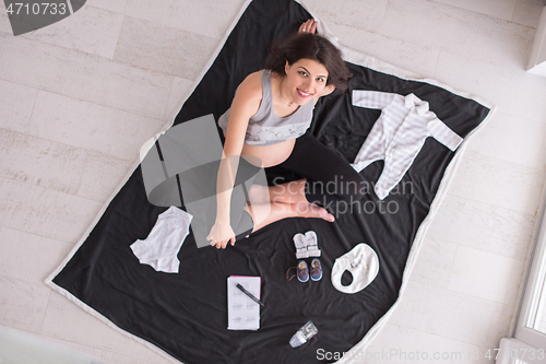 Image of top view of pregnant woman checking list of baby clothes