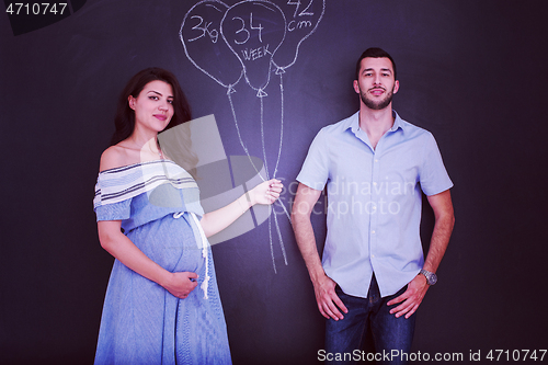 Image of pregnant couple drawing their imaginations on chalk board