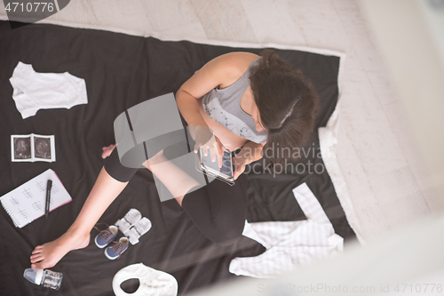 Image of top view of pregnant woman checking list of baby clothes