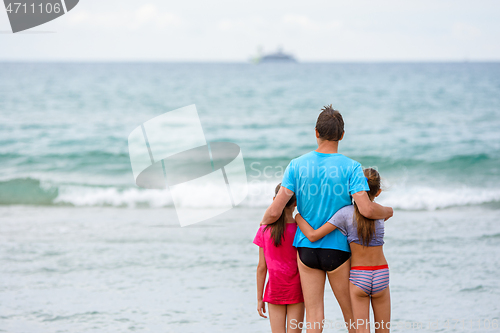 Image of Dad with two daughters are hugging on the seashore and looking into the distance