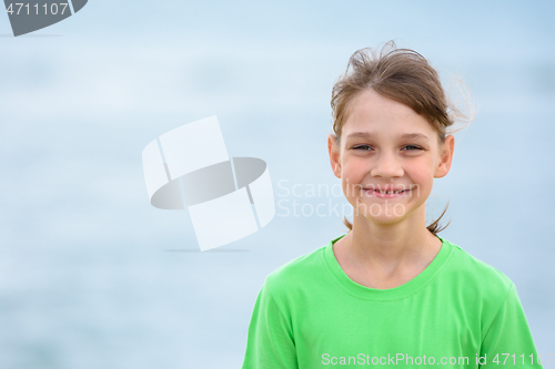 Image of Portrait of a happy ten-year-old girl in a green t-shirt on the background of the sea