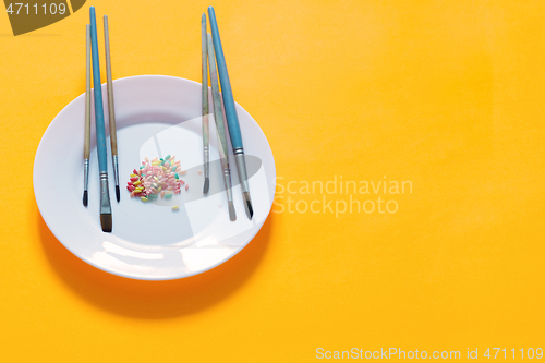 Image of Brushes and rice painted in different colors on a plate, yellow background