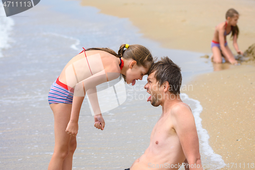 Image of Dad and daughter butt heads while sitting on the sea sandy shore