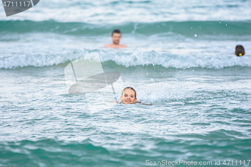 Image of A girl swims in the sea, several more people are swimming in the background