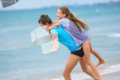 Image of Dad rolls his daughter on his back like on an improvised plane on the beach against the background of the sea