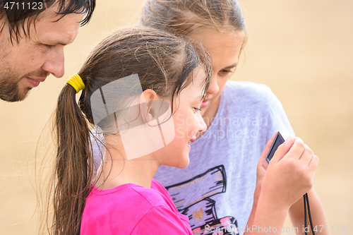 Image of Two girls and dad are looking at photos on the camera from a family beach vacation