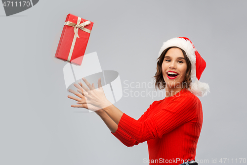 Image of happy young woman in santa hat catching gift box