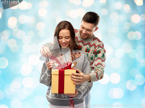 Image of happy couple in christmas sweaters with gift box