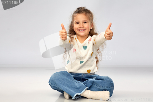 Image of little girl sitting on floor and showing thumbs up