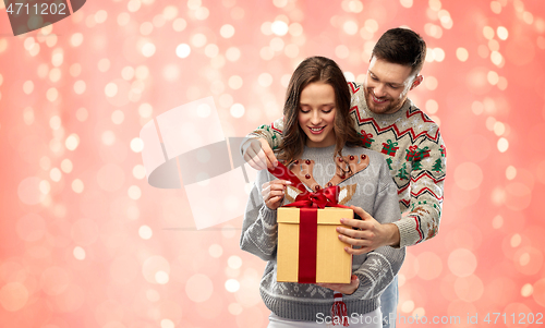 Image of happy couple in christmas sweaters with gift box