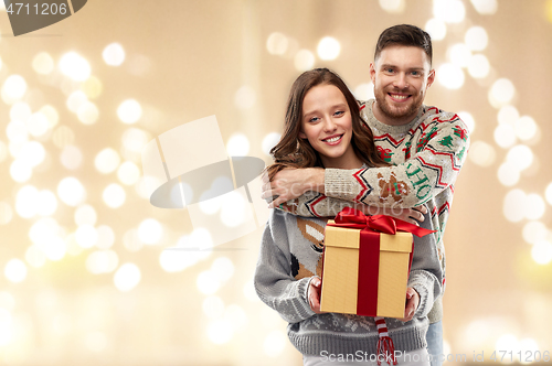 Image of happy couple in christmas sweaters with gift box