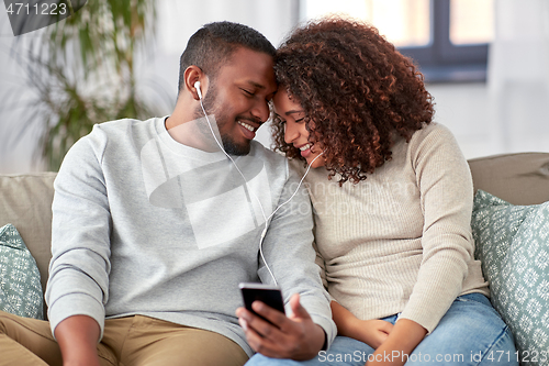 Image of happy couple with smartphone and earphones at home