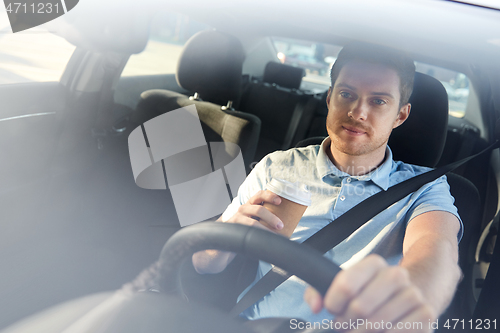 Image of tired man driving car with takeaway coffee