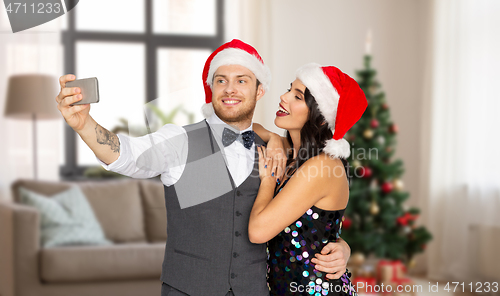 Image of couple in santa hats taking selfie on christmas