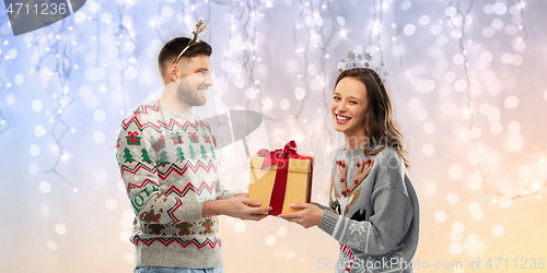 Image of happy couple in ugly sweaters with christmas gift