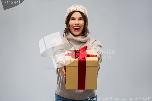 Image of young woman in knitted winter hat holding gift box
