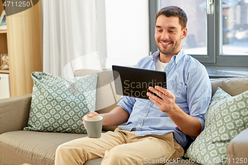 Image of smiling man with tablet pc drinking coffee at home