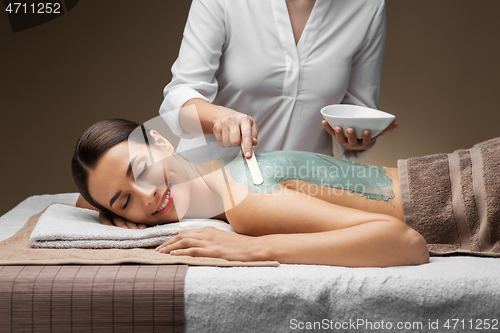 Image of woman and cosmetologist applying clay mask in spa