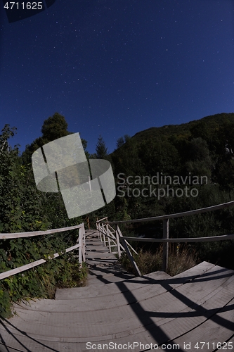 Image of wooden old bridge in forest over treetops in night with stars