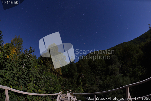 Image of wooden old bridge in forest over treetops in night with stars