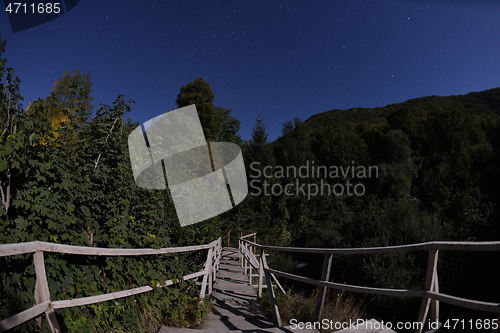 Image of wooden old bridge in forest over treetops in night with stars