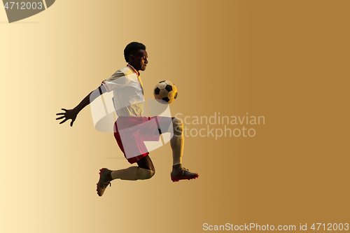 Image of Male soccer player kicking ball in jump isolated on gradient background