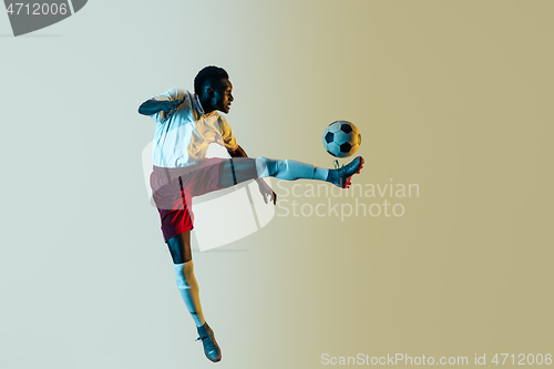 Image of Male soccer player kicking ball in jump isolated on gradient background