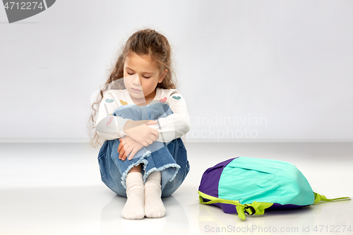 Image of sad little girl with school bag sitting on floor