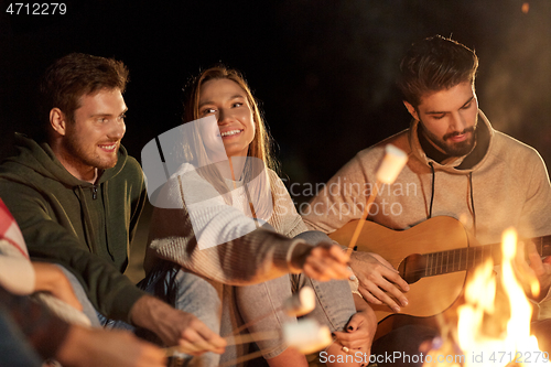 Image of friends roasting marshmallow and playing guitar