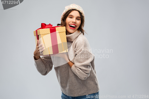 Image of young woman in knitted winter hat holding gift box