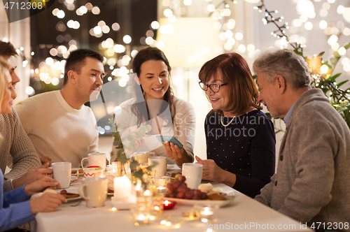 Image of happy family with smartphone at tea party at home