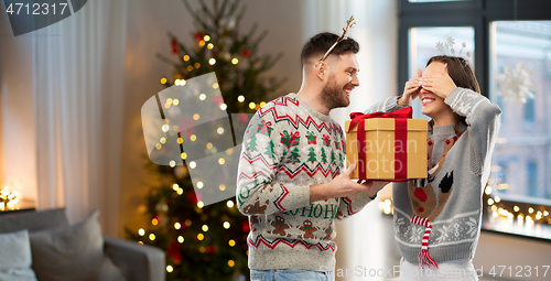 Image of happy couple in christmas sweaters with gift box