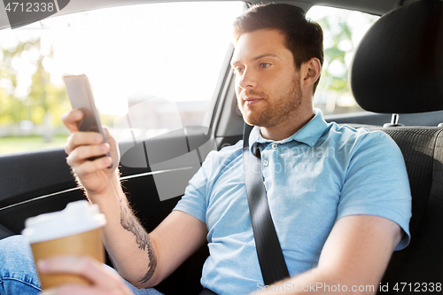 Image of passenger with coffee using smartphone in taxi car