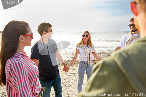 Image of happy friends holding hands on summer beach